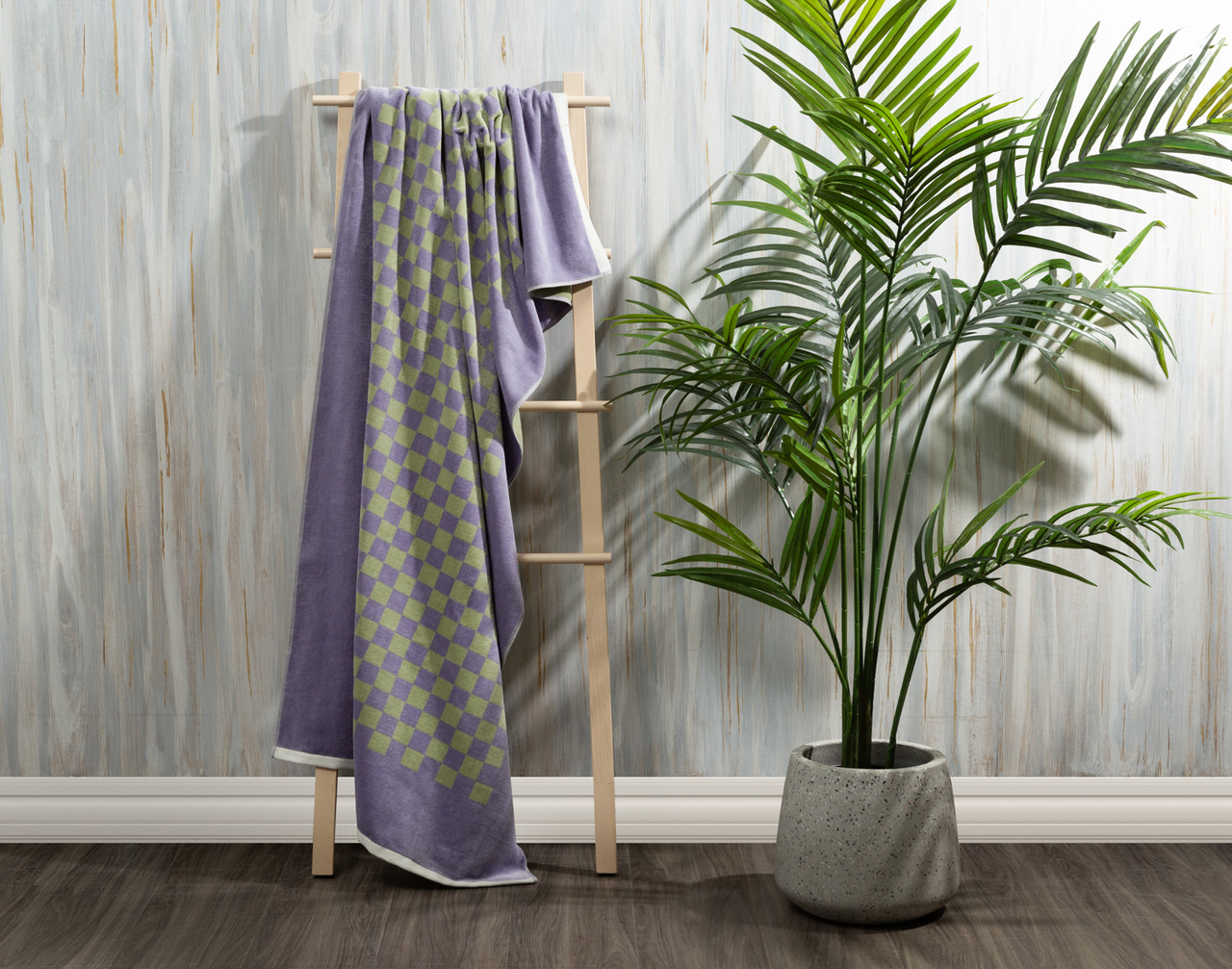 Our Checker Cotton Beach Towel draped over a hanging lattice next to a potted fern in a white room.
