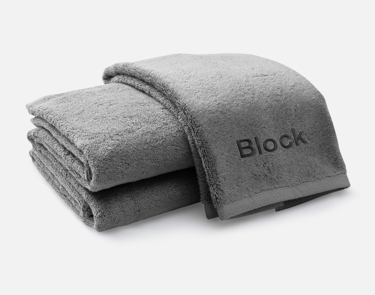 Vue pliée de notre serviette brodée personnalisée ensemble en gris, avec la police Block brodée en blanc noir le long du bord inférieur.