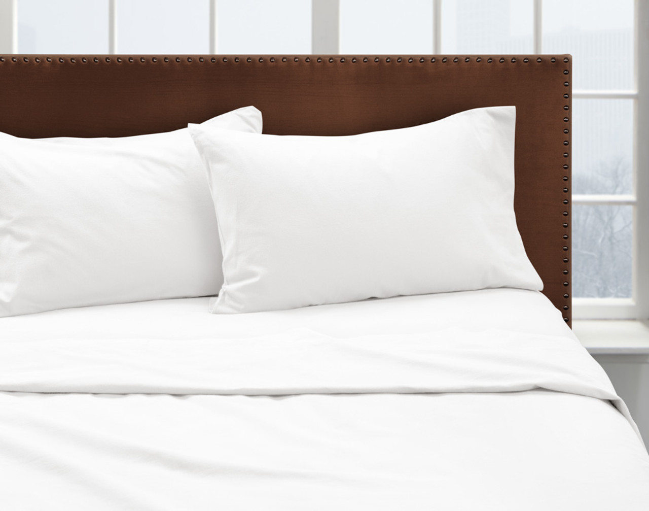 Vue de face de notre flanelle de coton biologique drap ensemble  en blanc, habillée proprement au-dessus d'un lit queen avec des oreillers queen dans une chambre à coucher blanche avec fenêtre.