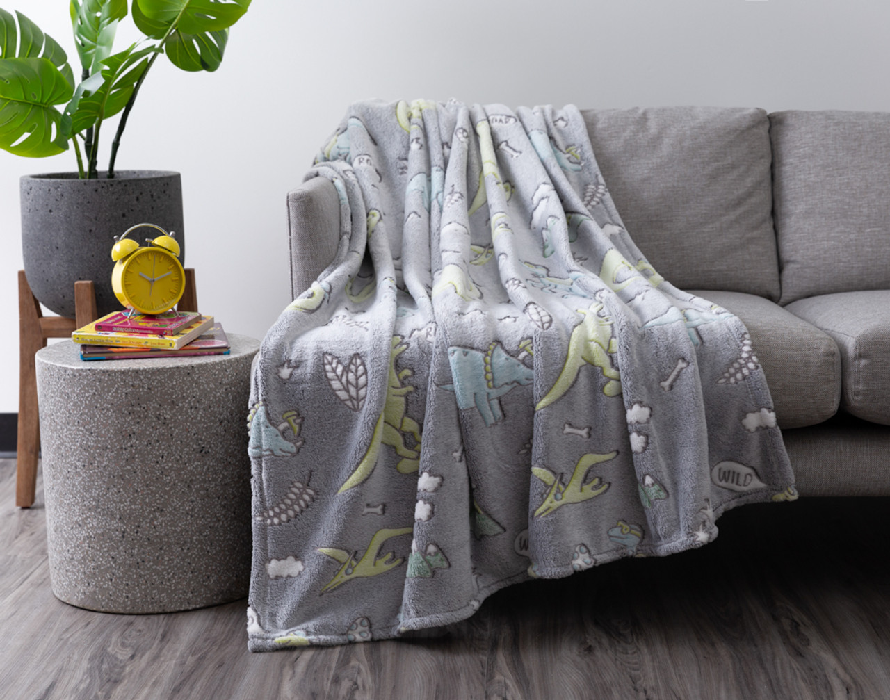 Our Dino Wild Glow in the Dark Fleece Throw draped over a grey couch in a modern living room.
