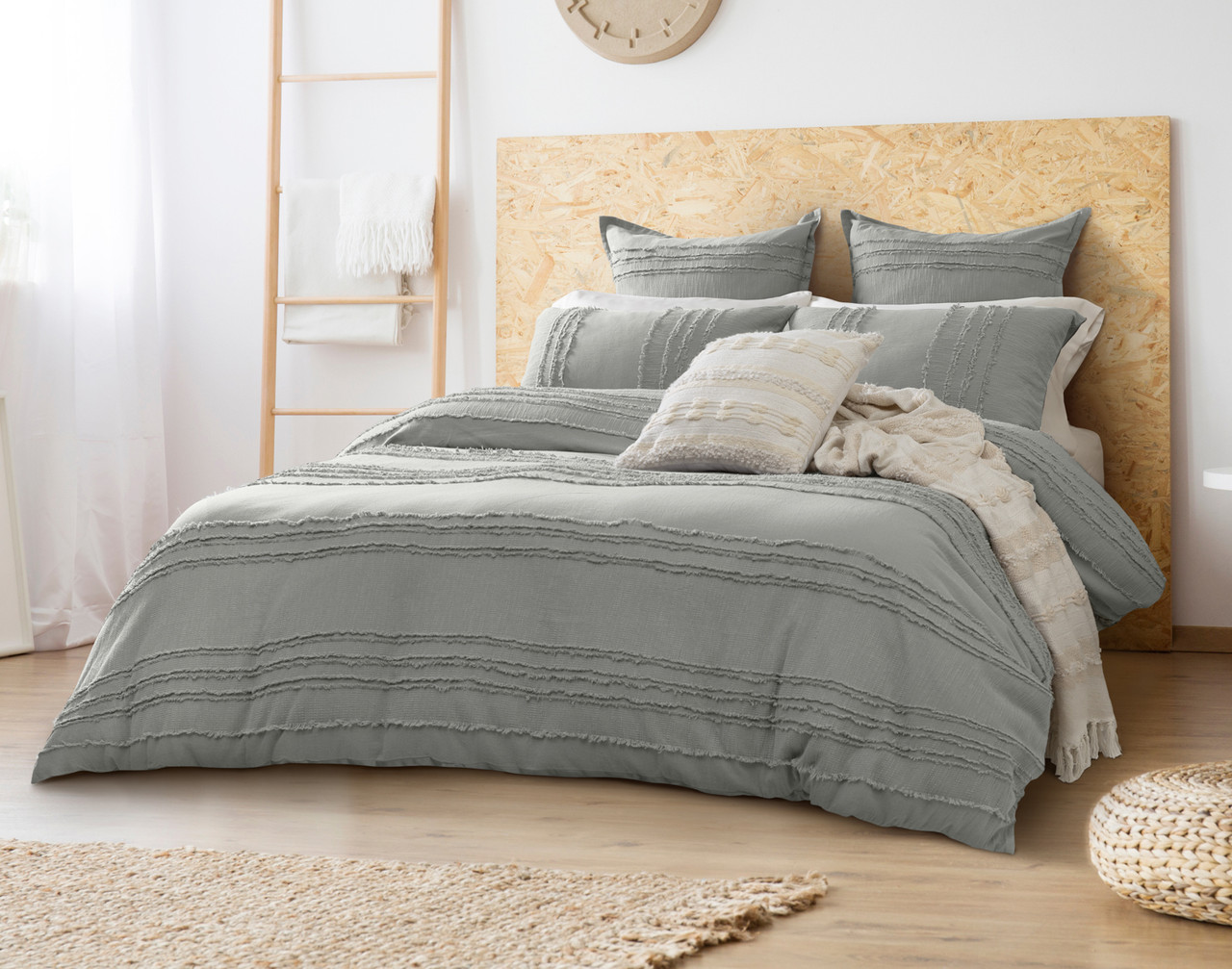 Vue en angle de notre housse de couette Hakai habillée sur un grand lit dans une chambre à coucher en bois blanc avec des coussins et des couvertures texturés.