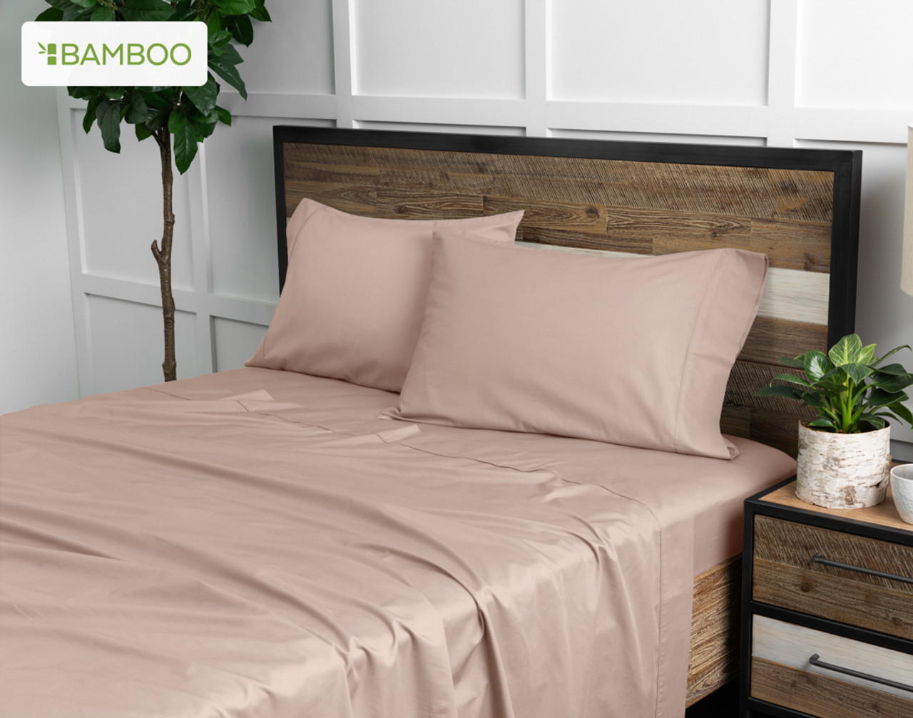 Angled view of our Bamboo Cotton Sheet Set in Frosted Berry dressed over a wooden bed in a white plant-filled bedroom.