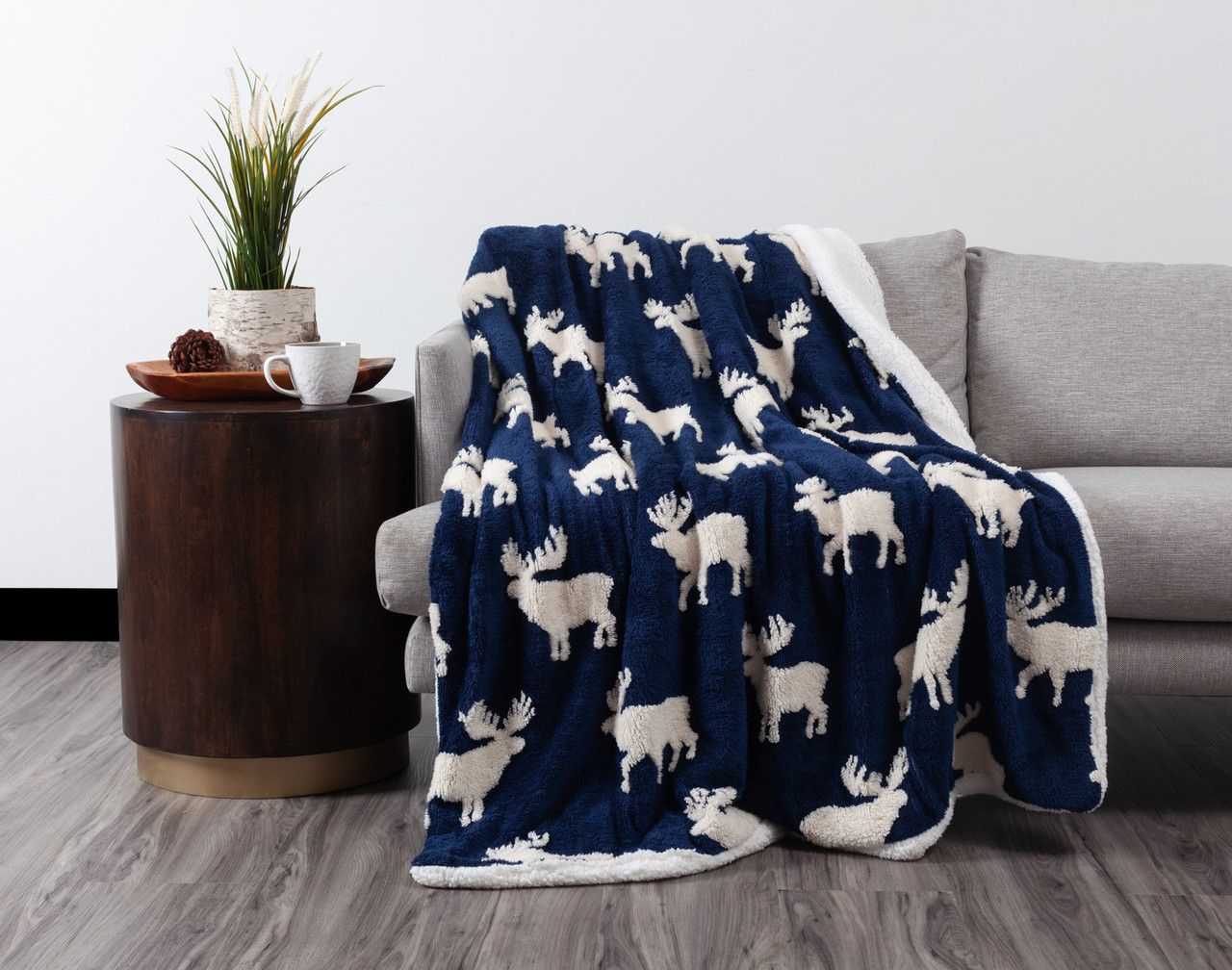 Front view of our Carved Holiday Throw in Moose Navy draped over the left side of a grey couch.