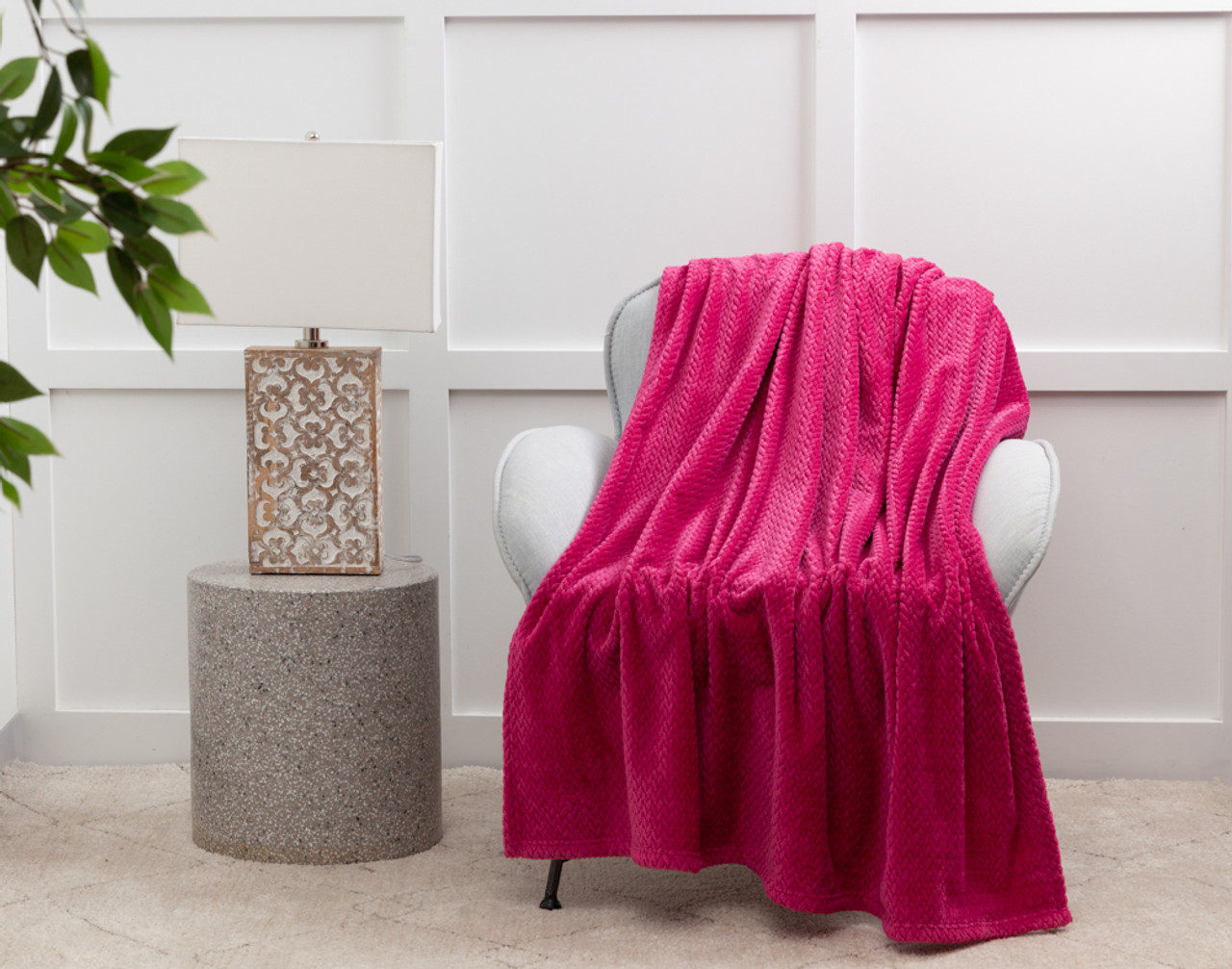 Notre peluche Chevron Jeté en Fuchsia sur une chaise blanche à côté d'une table de lampe.