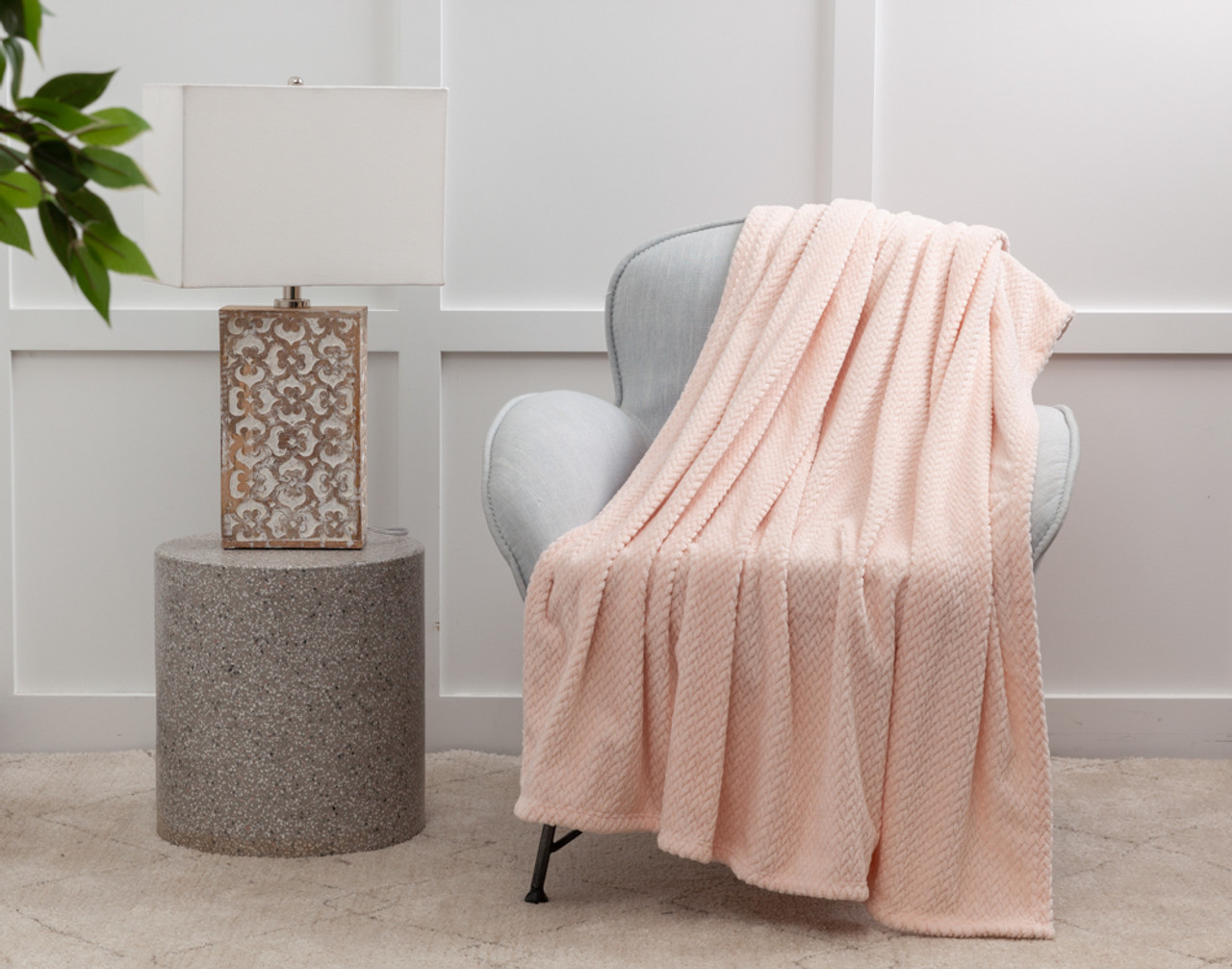 Our Chevron Plush Throw in Blush over a white chair next to an lamp table.