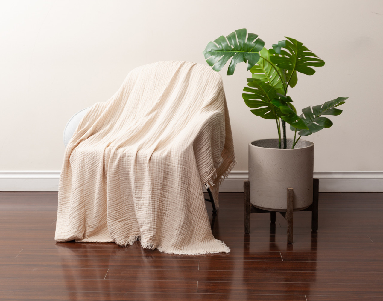 Angled view of our Muslin Gauze Throw in Natural draped over a chair next to a tall leafy plant.