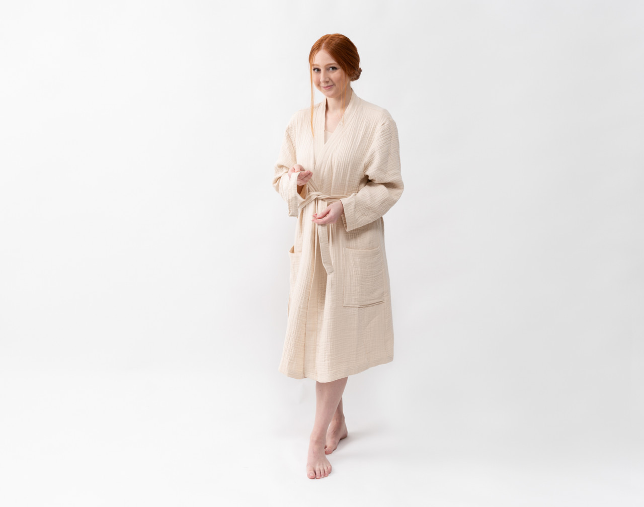 Front view of a woman wearing our Muslin Gauze Bathrobe in Natural standing in a solid white room.