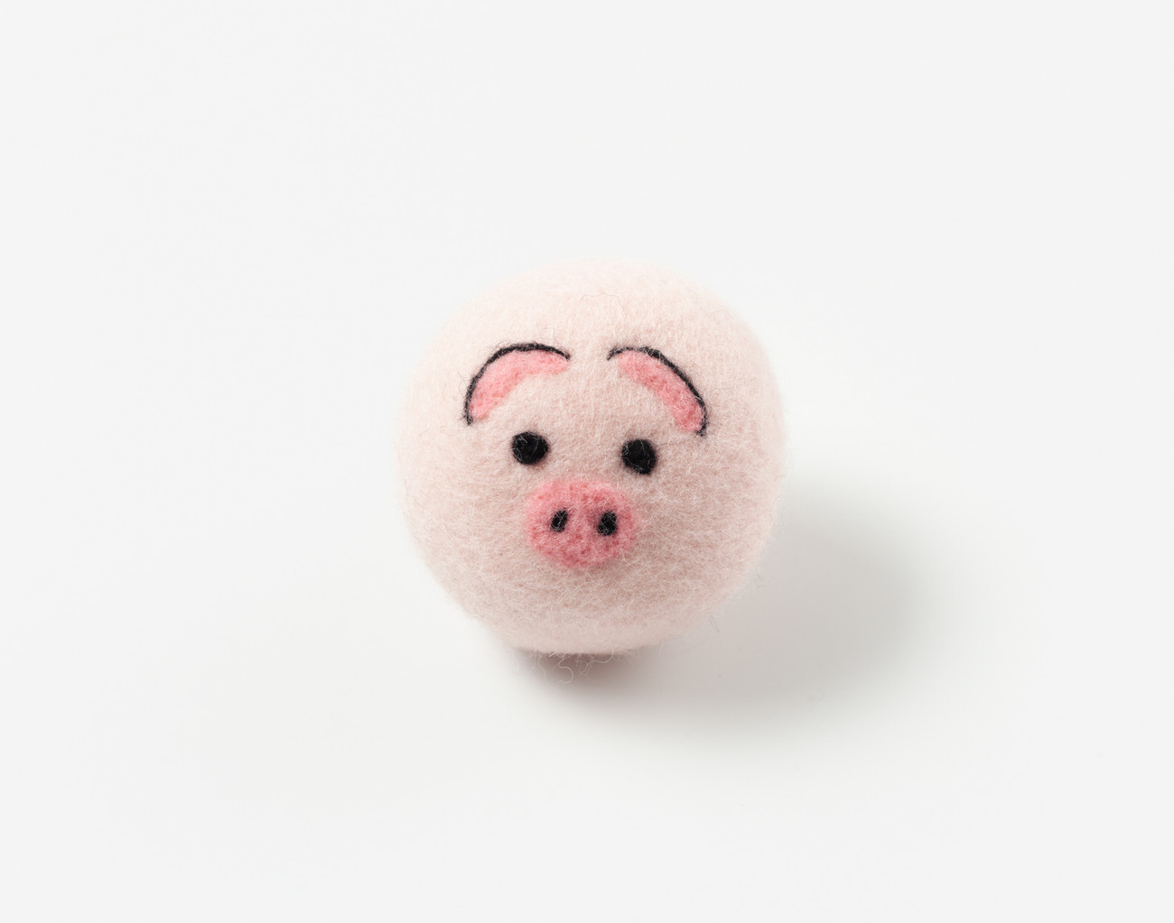 Vue de face de notre boule de séchage en laine brodée Piggy, posée sur une surface blanche solide.