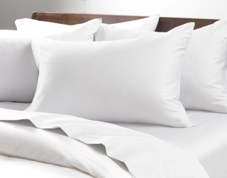 Angled view of four pillows in Cotton Blend Percale Pillowcases leaning against the headboard over a mattress.