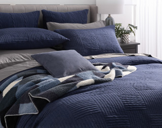 Angled side view of our Kye Duvet Cover Set dressing a queen bed with matching accessories and light grey sheets.