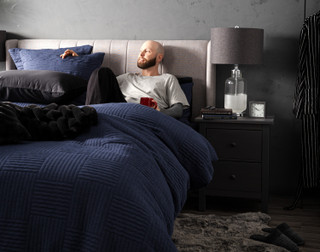 Front, off-centre view of a model lying in a bed dressed in our Kye Duvet Cover Set.