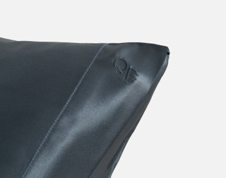 Close-up on the embroidered QE Home logo on the corner of our Mulberry Silk Pillowcase in Thundercloud.