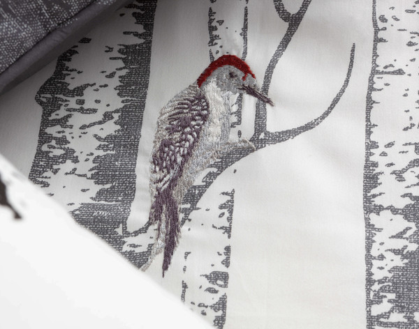 Close up of embroidered woodpecker in shades of red and grey.