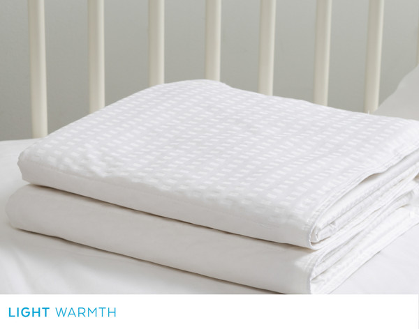 Our Petite Pearl Mulberry Silk Duvet folded in a gentle square on a mattress in a white crib.