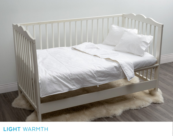 Our Petite Pearl Mulberry Silk Duvet over a white wooden crib in a white bedroom.