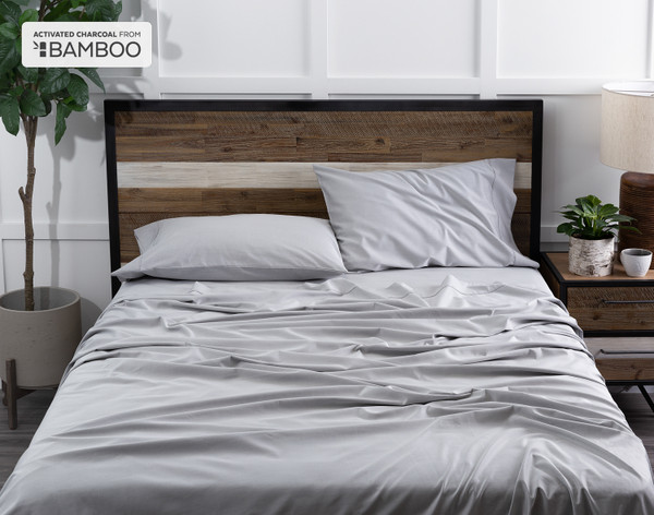 Top view of our Bamboo Cotton Sheet Set with Activated Charcoal dressed over a wooden bed in a white plant-filled bedroom.