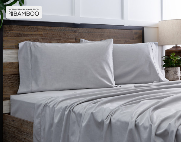 Deux de nos taies d'oreiller Bamboo Cotton avec charbon actif reposent sur un lit en bois avec draps coordonné.