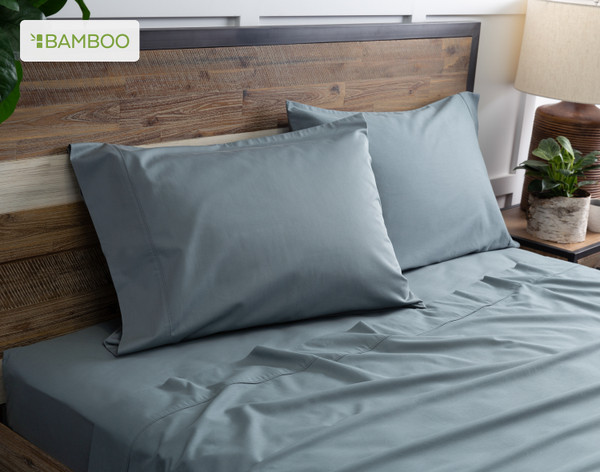 Deux de nos taies d'oreiller Bamboo Cotton en vert épicéa reposent sur un lit en bois avec draps coordonné.