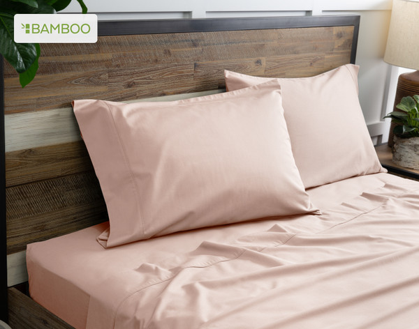 Two of our Bamboo Cotton Pillowcases in Blush Pink resting on a wooden bed with coordinating sheets.