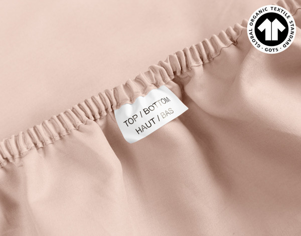 Gros plan sur le tissu de coton sensationnellement doux et l'étiquette Top & Bottom sur le bord de notre Organic Cotton Fitted drap en Rose Smoke.