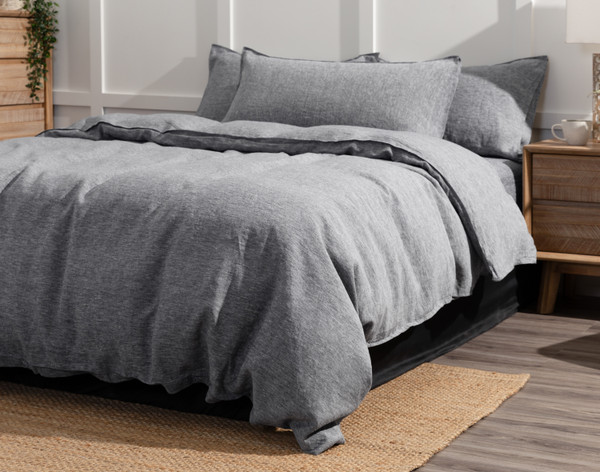 Vue en angle de notre housse de couette Signature European Linen en Indigo Grey habillée d'un grand lit dans une chambre à coucher blanche avec un sol et des meubles en chêne marron.
