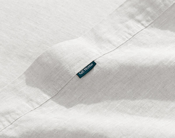 Close-up on the hemmed edge and small QE Home tag on the border of our Signature European Linen Flat Sheet in White.