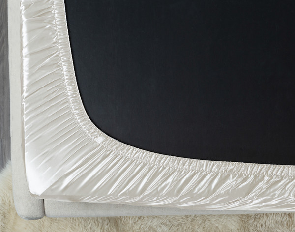 Underside of a black mattress wearing our Mulberry Silk Fitted Sheet in White Snow to show its elastic.