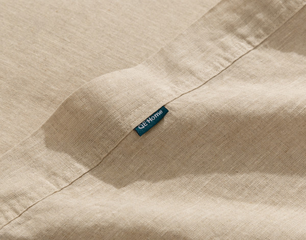 Gros plan sur le bord ourlé et la petite étiquette QE Home sur la bordure de notre Signature European Linen Flat drap en Natural.