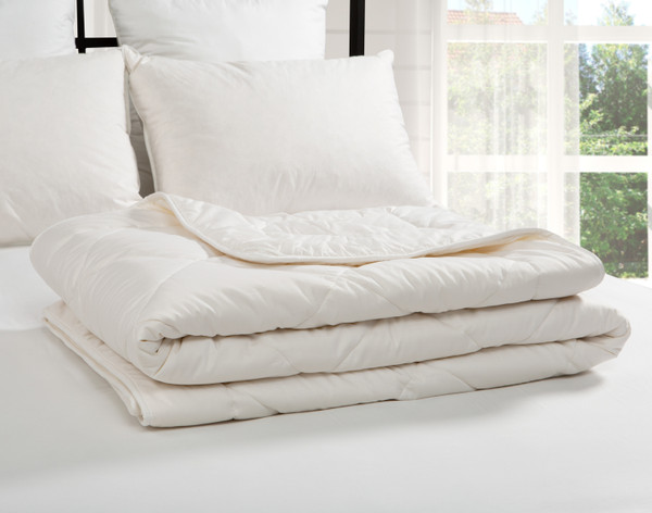 Notre couette Affinity en laine australienne s'est pliée délicatement en un carré bien rangé sur le dessus d'un lit blanc.