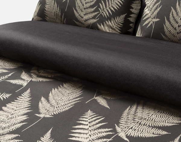 Angled view of the folded top edge on our Nightfall Duvet Cover to show its antique gold fern pattern and solid black reverse.