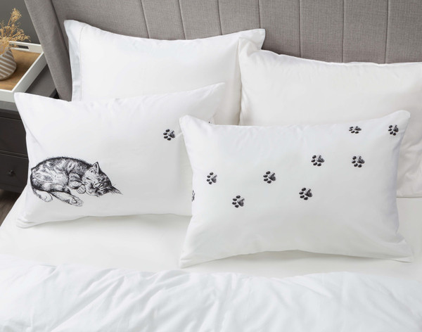 Vue en angle de nos taies d'oreiller Sleeping Cat posées sur un lit blanc à moitié habillé.