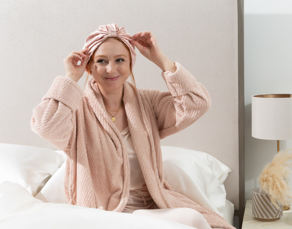 Femme en robe de chambre portant notre enveloppe de cheveux Soie de mûrier . rose blush , assise bien droite dans son lit.