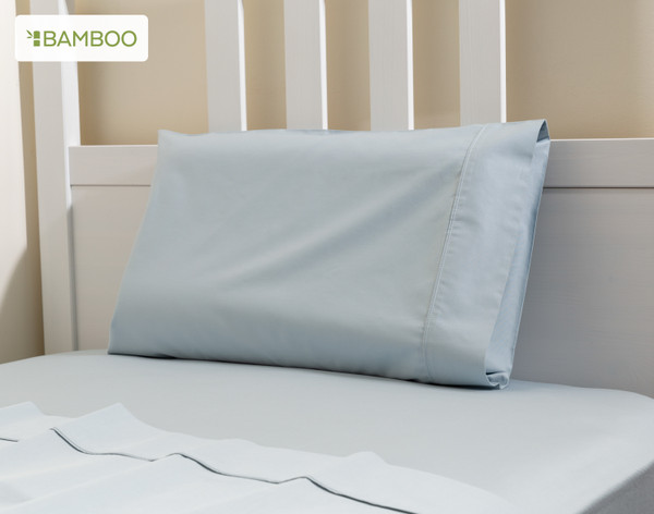 Angled view of our Small Bamboo Cotton Pillowcase in Sky Blue leaning against the headboard of a children's white bed.