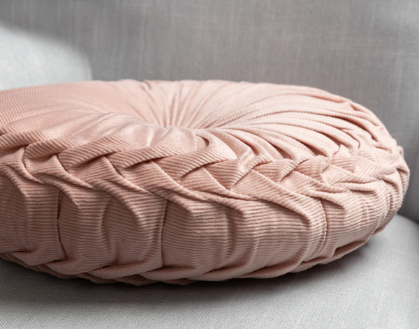 Vue latérale de notre coussin rond en velours côtelé Pin-Tuck sur rose blush pour montrer son bord plissé détaillé.