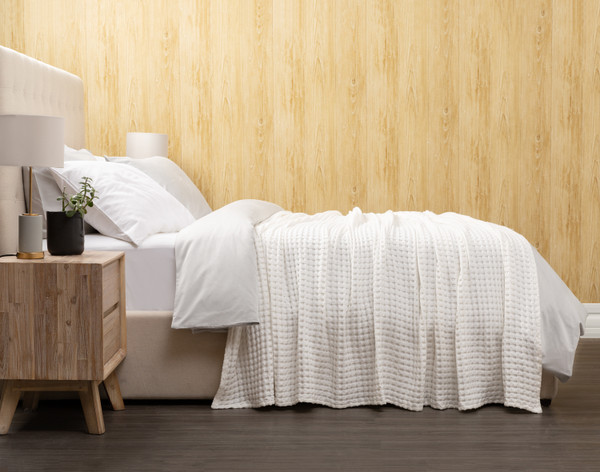 Vue latérale de notre couverture gaufrée Bamboo Cotton en ______ habillée proprement au-dessus d'un grand lit dans une chambre à coucher en bois.
