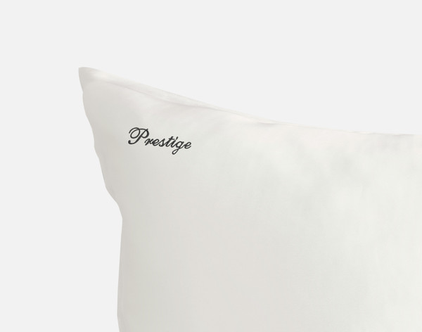 Close-up of the corner on our Snow White Mulberry Silk Pillowcase, featuring the word "Prestige" embroidered in black thread in our cursive Prestige font.