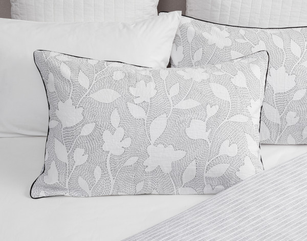 Our Shyla Pillow Sham resting against coordinating white pillows on a half-dressed white bed.