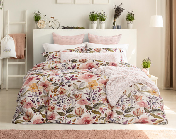 Vue de face de notre housse de couette Marsala habillée sur un grand lit, accessoirisée de divers coussins blancs et roses dans une chambre blanche remplie de plantes.