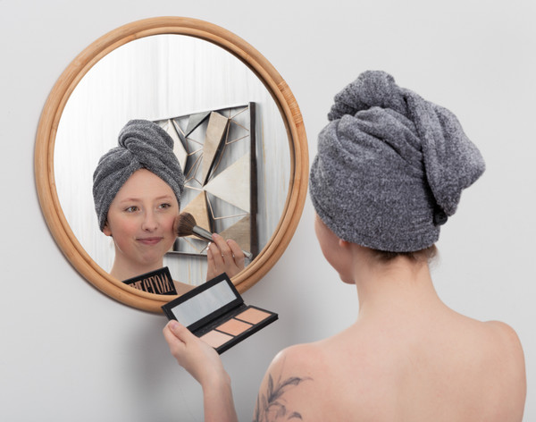 Young woman applying blush in front of a mirror while her hair is wrapped in our Charcoal Infused Cotton Hair Wrap.