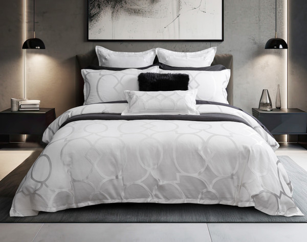 Vue de face de notre housse de couette Avenue dans une chambre à coucher moderne grise, recouverte de divers coussins noirs et blancs.