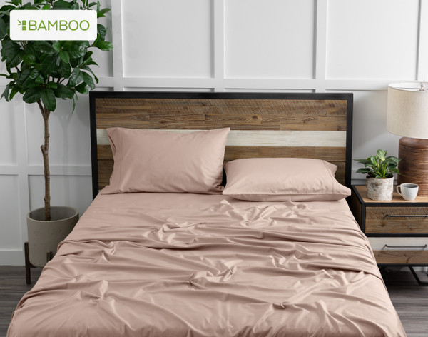 Front view of our Bamboo Cotton Sheet Set in Frosted Berry dressed over a wooden bed in a white plant-filled bedroom.