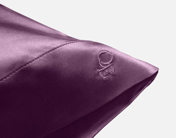 Close-up on the embroidered QE Home logo on the corner of our Mulberry Silk Pillowcase in Plum.