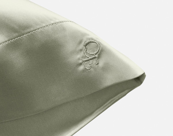 Close-up on the embroidered QE Home logo on the corner of our Mulberry Silk Pillowcase in Mistywoods.