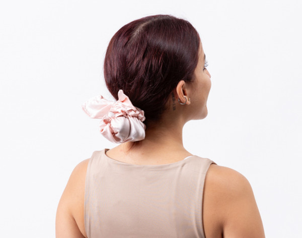 Rear view of a woman wearing our Mulberry Silk Bun Cover in Blush tied around her hair in a compact bun.