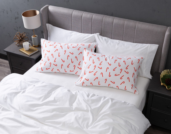 Angled view of our Candy Canes Pillow Talk Pillowcases sitting on a white bed in a dark grey bedroom.