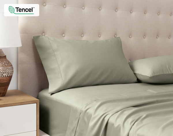 Vue en angle de nos Taies d'oreiller Eucalyptus Luxe TENCEL™ Lyocell en Mistywoods posées contre la tête de lit d'un lit queen beige.