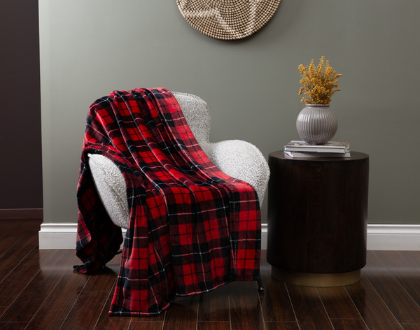 Angled view of our Plaid Throw in Crimson draped over a small armchair in a green living room.