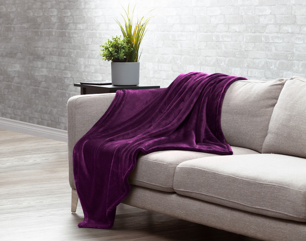 Our Velvet Plush Throw in Purple draped over a beige couch in a white living room.