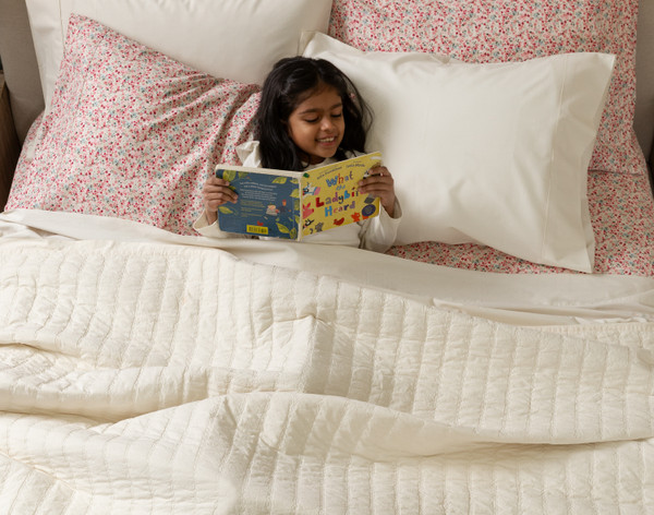 Front view of a young girl reading a book in a bed dressed in our Ivory and Carefree Cotton Caress Sheets.