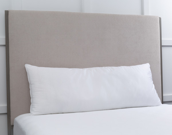 Angled view of our Essential Body Pillow sitting on an empty white bed against a beige headboard.